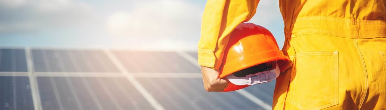 O3_Solar worker holding helmet looking at panels Solar employee holding their helmet, facing a solar panel.