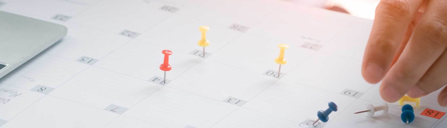 Person putting pins on dates listed on a calendar