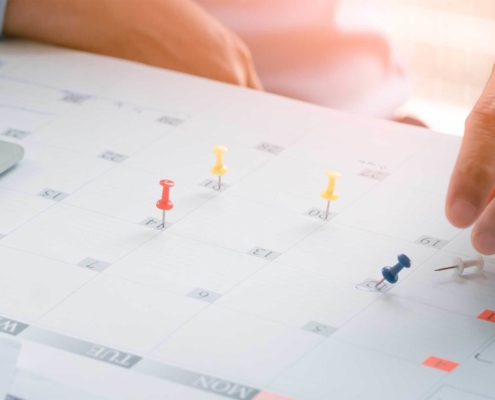 Person putting pins on dates listed on a calendar