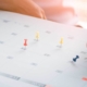 Person putting pins on dates listed on a calendar
